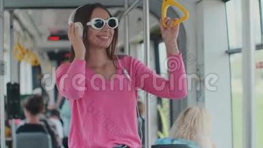 一位戴着耳机站在现代电<strong>车上</strong>的年轻女子的特写肖像。 戴眼镜的女人用眼镜听<strong>音乐</strong>